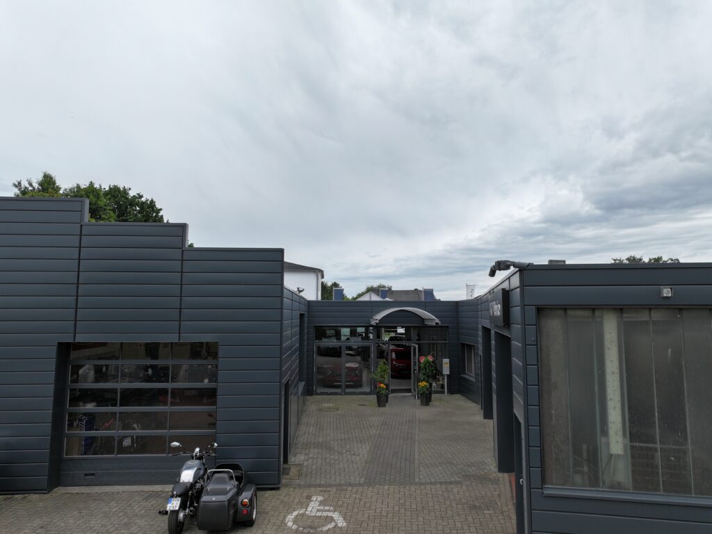 Eingangsbereich des Autohaus Hakelberg mit moderner grauer Fassade, Glasfront und Motorrad mit Beiwagen im Vordergrund.