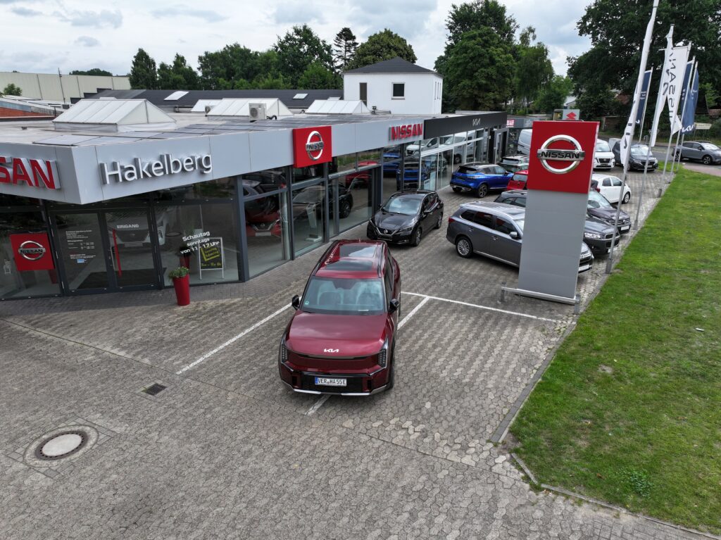 Autohaus Hakelberg in Verden mit Nissan-Showroom und ausgestellten Fahrzeugen, darunter ein roter Kia auf dem Parkplatz.