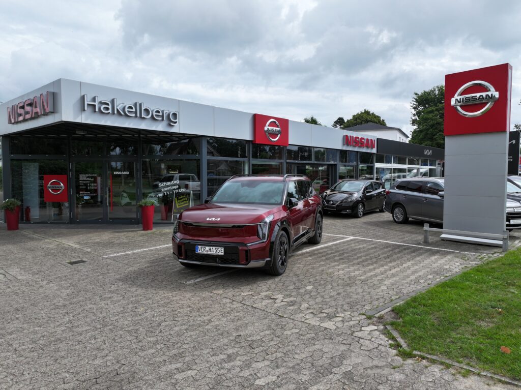 Autohaus Hakelberg in Verden mit Nissan-Showroom und ausgestellten Fahrzeugen, darunter ein roter Kia auf dem Parkplatz.