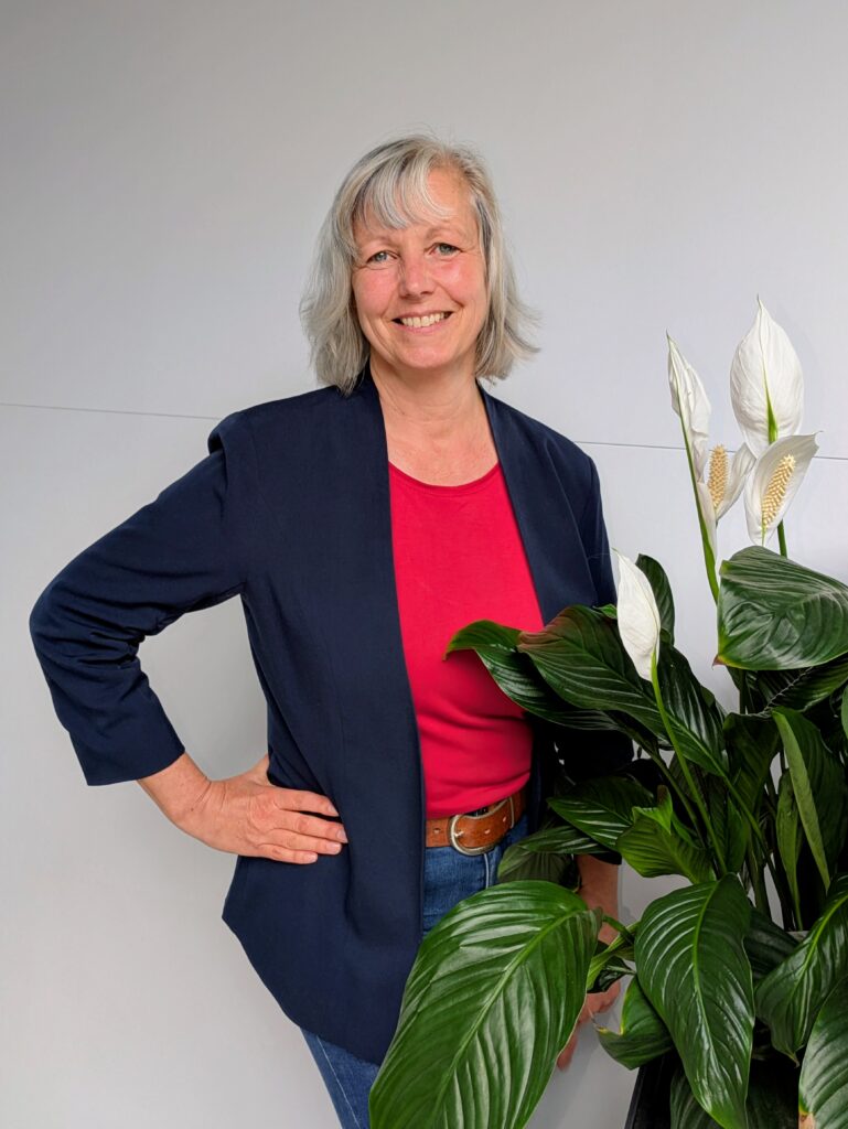 Portraifoto der Eigentümerin lächelt neben einer Pflanze in die Kamera