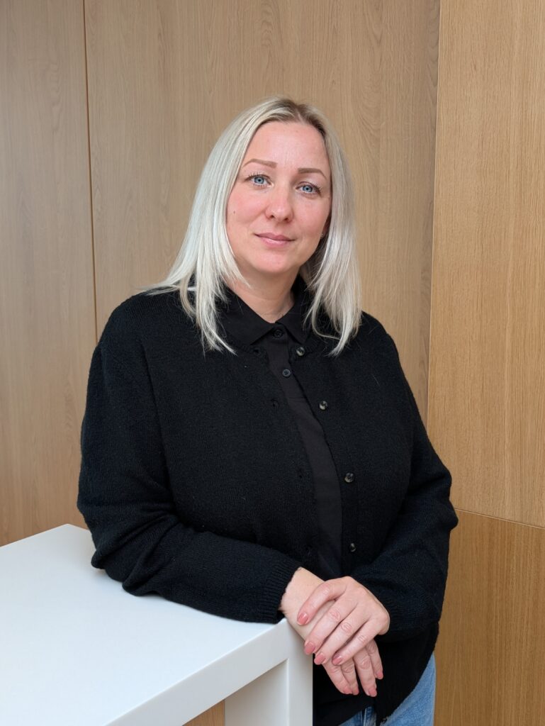 Eine Mitarbeiterin an einen Verkaufstresen angelehnt lächlt in die Kamera