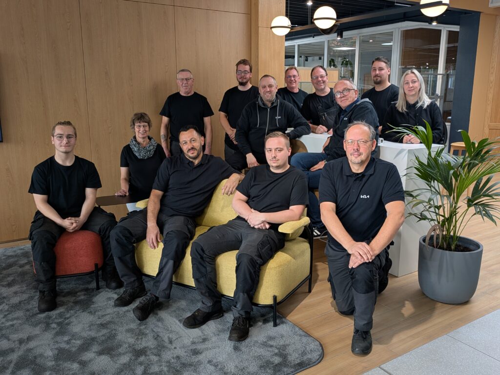 Teamfoto der Mitarbeiter im Autohaus KIA Hakelberg in modernem Showroom mit Holz- und Pflanzenelementen.